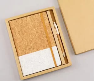 Two-tone natural cork and white linen hardcover notebook with a matching cork pen packaged in an eco-friendly kraft paper gift box.