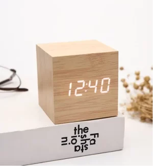 Modern minimalist wooden cube digital desk clock displaying white LED time on a white surface next to a book.