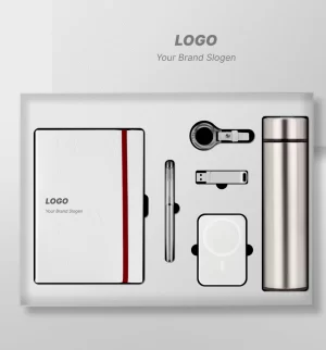 Premium customized executive corporate gift set laid out in a white presentation box, featuring a white notebook with a red elastic band, a sleek metal pen, a USB flash drive, a multi-connector charging cable, a wireless power bank, and a stainless steel thermal water bottle.