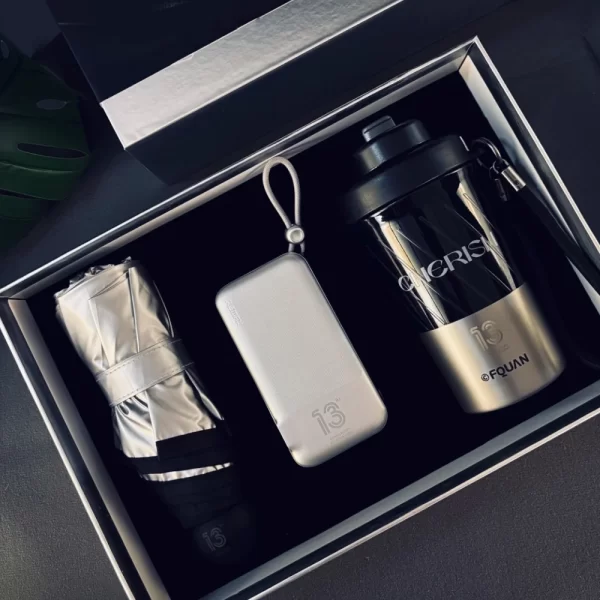 Premium Vacuum Cup Business Gift Set with Everyday Lifestyle Accessories Luxury corporate gift box set featuring a stylish vacuum tumbler with "CHERISH" branding, a compact metallic silver power bank with a lanyard, and a folded silver compact umbrella arranged neatly in a dark presentation box.