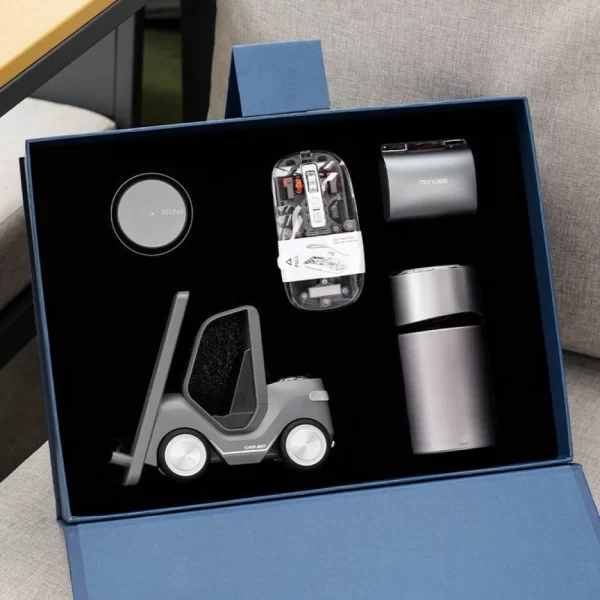 Kinetic Performance Mastery Executive Modern Workspace Tech Gift Box Set Open navy blue gift box with black foam insert featuring a matte grey forklift-shaped desk organizer and phone stand, a transparent tech mouse, a sleek metallic thermal tumbler, a round magnetic wireless charger, and a modern desk accessory.